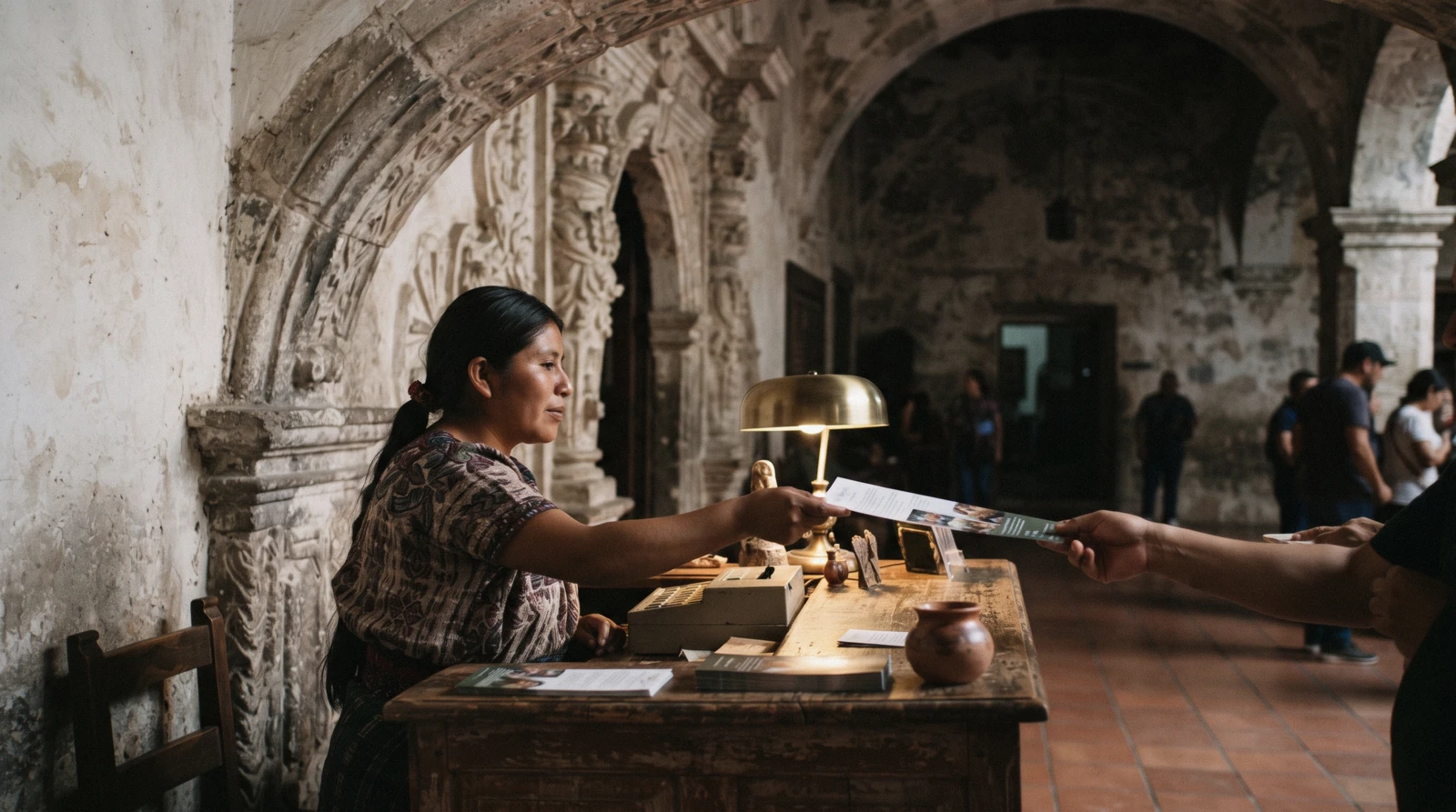 The museum ticket desk inside the Santo Domingo monastery complex in Antigua Guatemala under a carved stone arch, warm lamp light